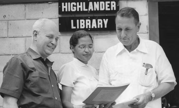 A black and white photo of Highlander founder Myles Horton (right) with civil rights leader Rosa Parks in front of a sign reading Highlander Library