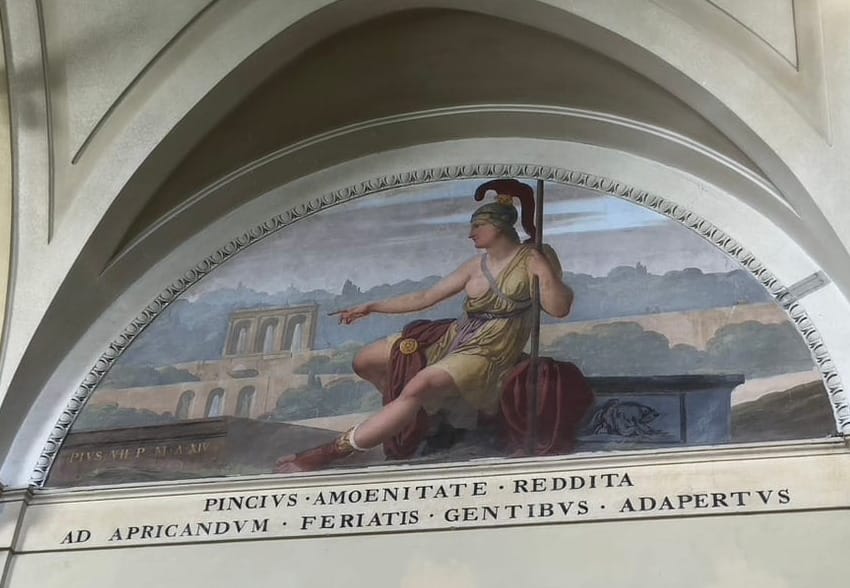 A woman in a tunic with one breast exposed, a war helmet, boots, and a spear points back toward a colonnade in the background. An inscription reads PINCIUS AMOENITATE REDDITA AD APRICANDUM FERIATIS GENTIBUS ADAPERTUS