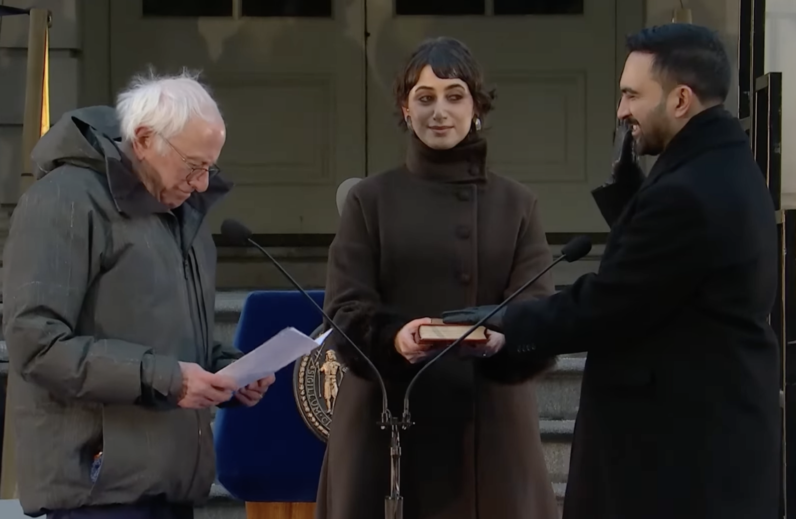 Bernie Sanders, left, reads the oath of office to be repeated by Zohran Mamdani, right, who is holding his right hand up and his left on two Qurans held by his wife Rama Duwaji