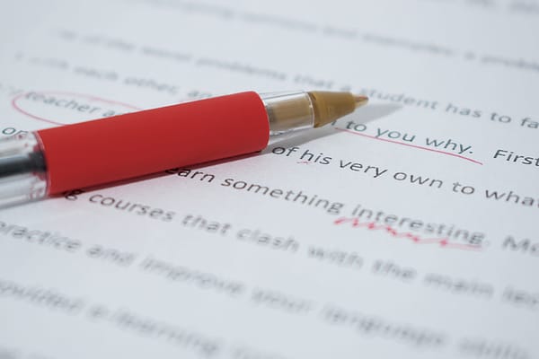 A red pen lying on a printed essay with some words circled and underlined